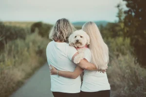 Duas pessoas abraçadas ao ar livre enquanto seguram um cachorro branco no colo.