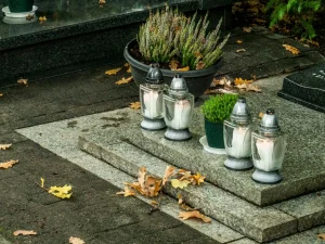 Velas acesas e vasos com plantas sobre um túmulo em um cemitério.