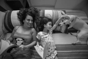 Mulher e criança deitadas na cama lendo livros enquanto fazem carinho em um cachorro ao lado, em um momento de convivência em família.