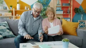 Casal idoso analisando documentos e dinheiro em casa.