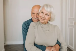 Casal de idosos sorrindo e se abraçando em um ambiente residencial.