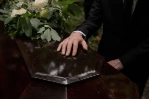 Homem de terno com a mão apoiada sobre um caixão durante uma cerimônia fúnebre.