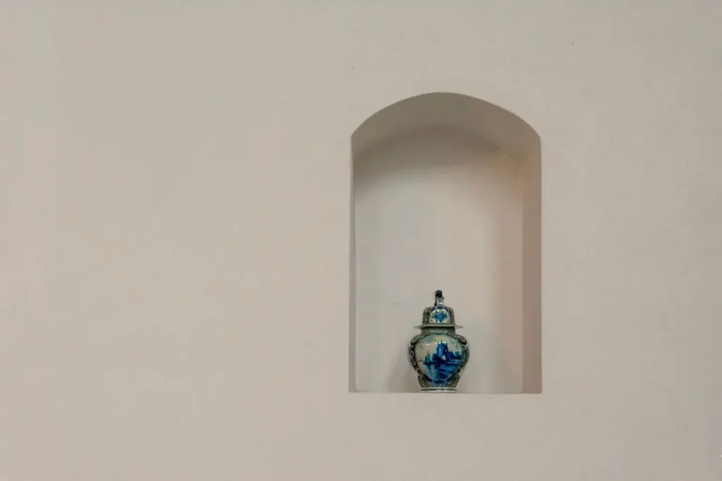 Urna funerária posicionada em um nicho de parede branca.
