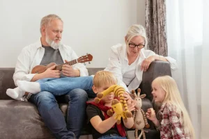 Idosos brincam com os netos na sala enquanto o avô toca ukulele.